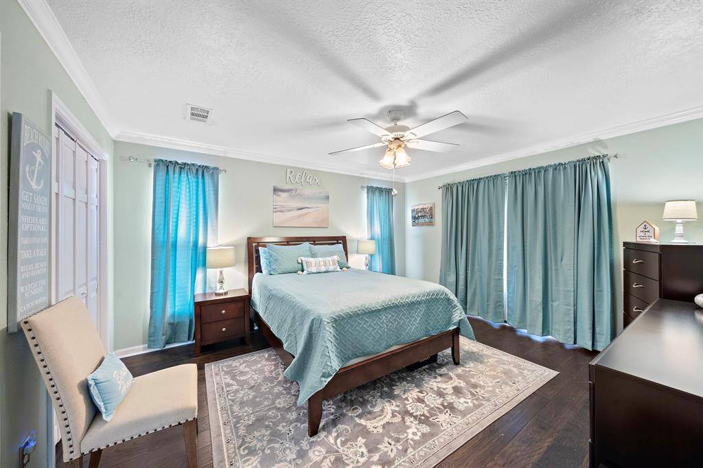 Spacious primary bedroom tastefully decorated in a sophisticated coastal color palette. French doors beyond the curtains on the right access the wraparound porch.
