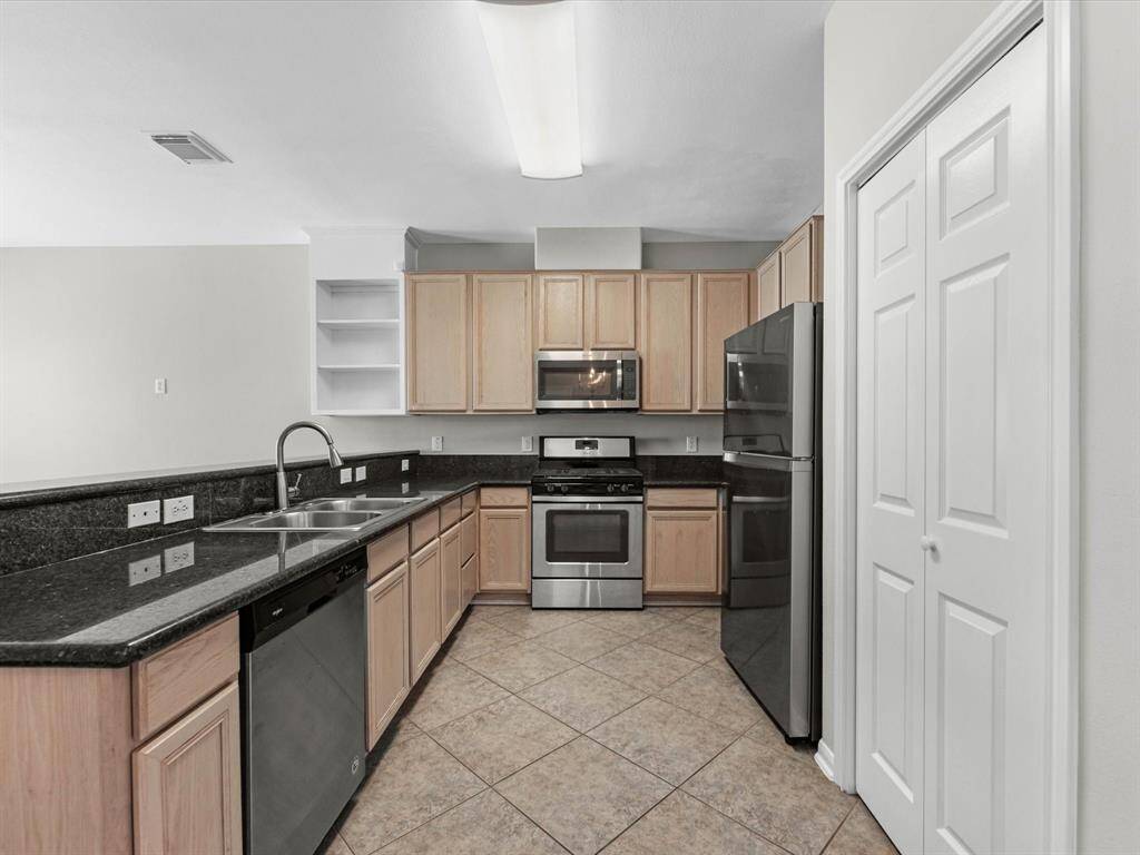 Modern kitchen with stainless steel appliances and granite countertops, complemented by tile flooring and a neutral color palette. The pantry is through the door to the right.