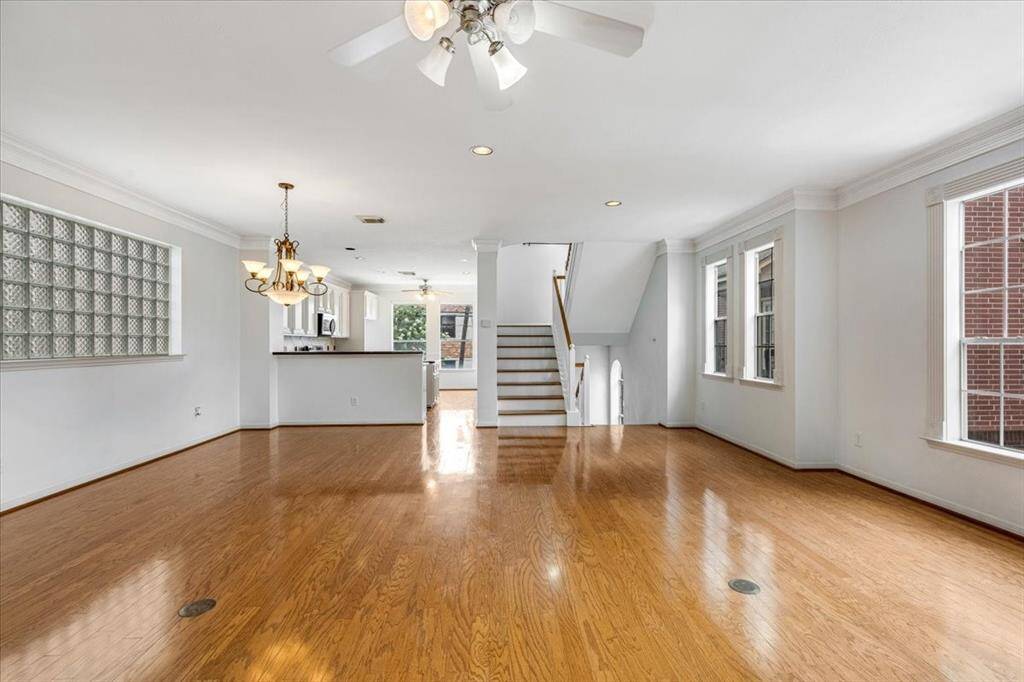 View from the living area toward the dining space and kitchen, highlighting the open layout, hardwood flooring, crown molding, and staircase leading up and down.