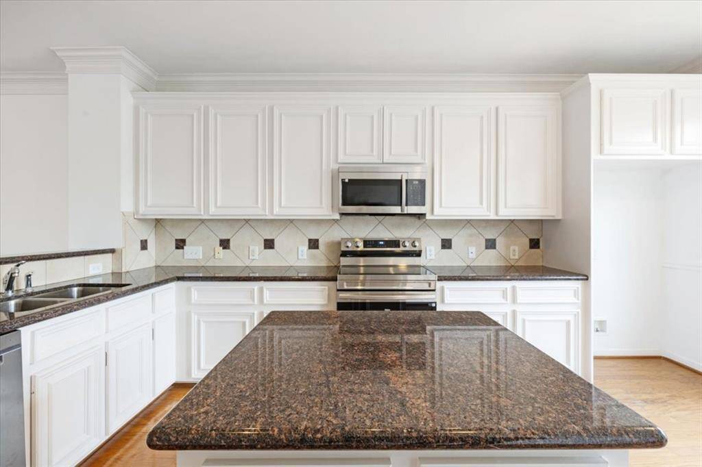 Chef-inspired kitchen with granite counters, white cabinetry, stainless steel appliances, and a functional island for meal prep.