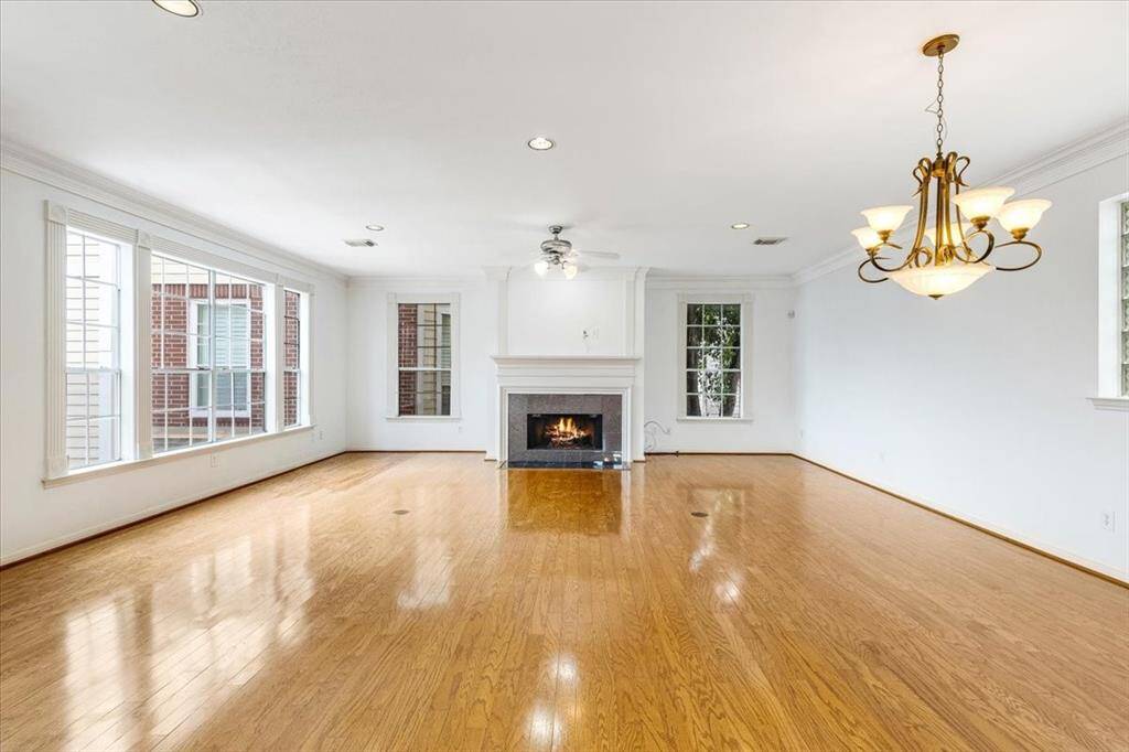Expansive second-floor living room with hardwood floors, a cozy fireplace, recessed lighting, and oversized windows that fill the space with natural light.