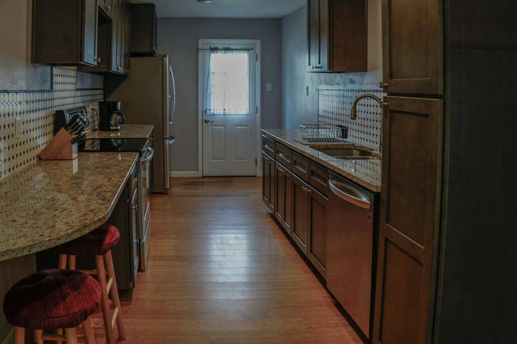 Kitchen with breakfast counter, stainless dishwasher, refrigerator and a door to side yard.