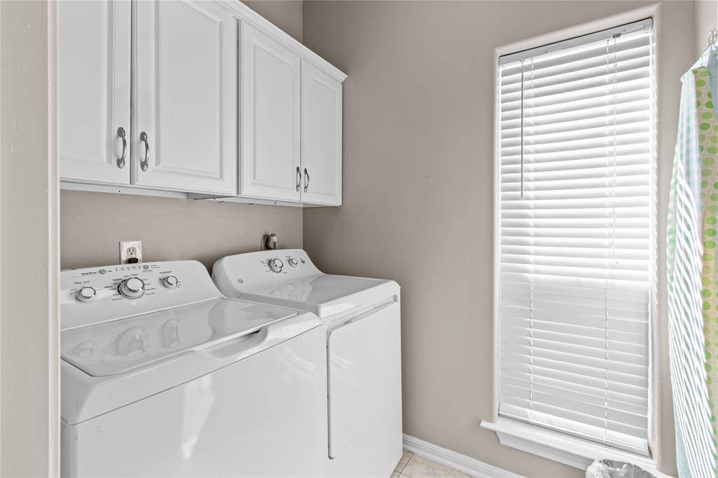 Utility room located on the first floor featuring a washer and dryer set, white cabinetry for storage, and a window with blinds allowing natural light.