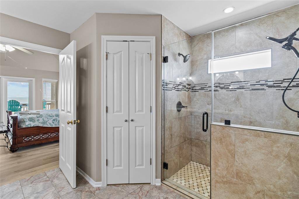 This photo showcases a modern bathroom with a glass-enclosed shower featuring stylish tilework. Adjacent is a doorway leading to a bedroom with a view, highlighting the home's open and airy design.