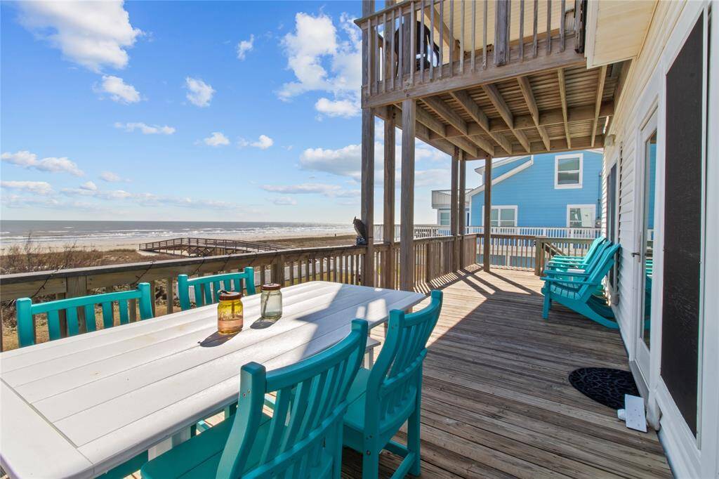 This photo showcases a beachfront deck with ocean views, featuring a spacious wooden patio with turquoise chairs and a dining table, perfect for outdoor relaxation and entertaining.