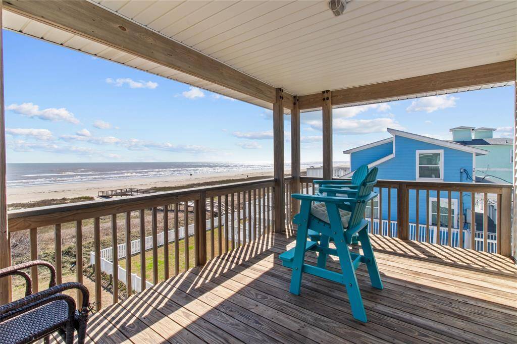 This photo showcases a covered wooden deck with ocean views, featuring a turquoise chair and wicker seating. It's perfect for relaxing and enjoying the beachside ambiance.