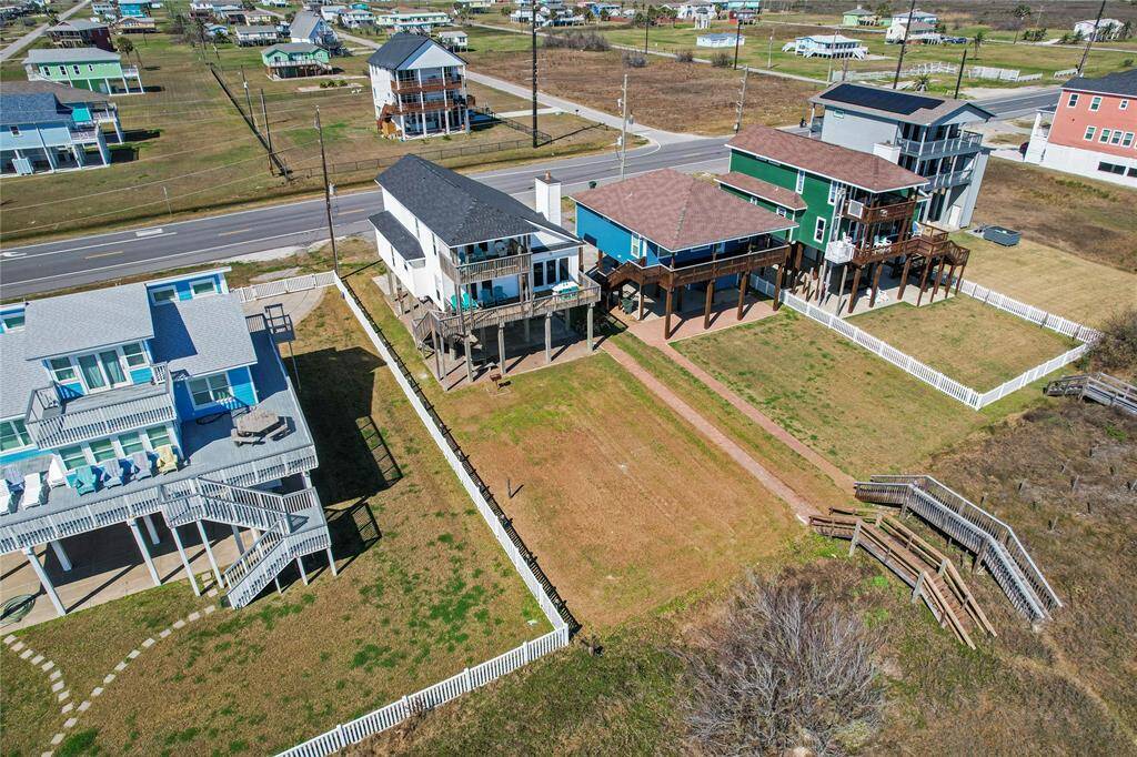 This photo showcases a covered outdoor area beneath a raised house, featuring sturdy wooden pillars, a staircase, and a mix of concrete and brick flooring. Ideal for parking or storage, it includes a patio area, outdoor shower, and a fenced yard, offering functionality and outdoor enjoyment.