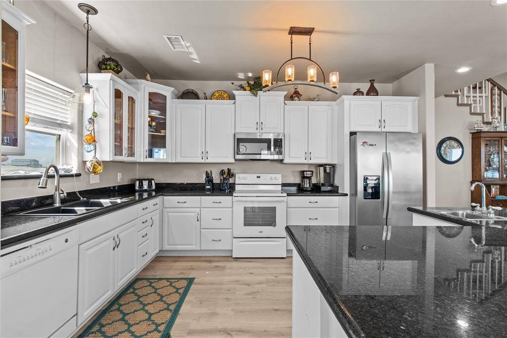 This kitchen features sleek black granite countertops, modern stainless steel appliances, and ample white cabinetry. The large island offers additional workspace and seating, while pendant lighting adds a stylish touch. The open layout enhances functionality and flow.
