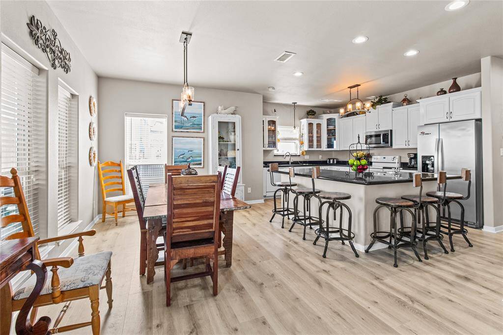 This open-concept living space features a modern kitchen with a large island and granite countertops, seamlessly connected to a cozy living room with a fireplace. The dining area is bright with natural light, thanks to multiple windows, and offers views of the outdoors. The space combines functionality with a warm, inviting ambiance.