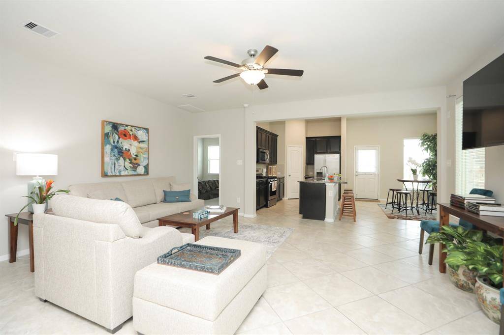 Bright and open living space with neutral tones, featuring a comfortable seating area, modern kitchen with dark cabinetry, and dining nook. Tile flooring and ceiling fan enhance the airy feel. Perfect for entertaining.