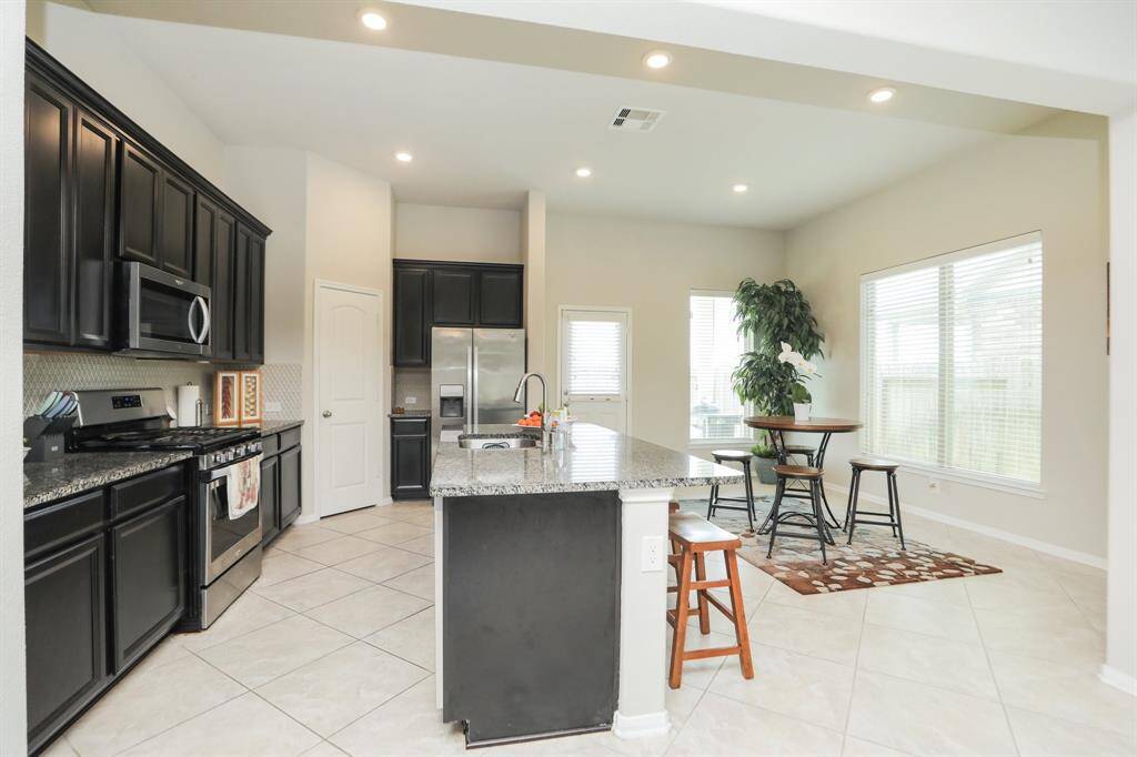 Bright, modern kitchen with dark cabinetry, granite countertops, and stainless steel appliances. Open layout includes a kitchen island with seating and a cozy dining area by large windows, offering plenty of natural light.
