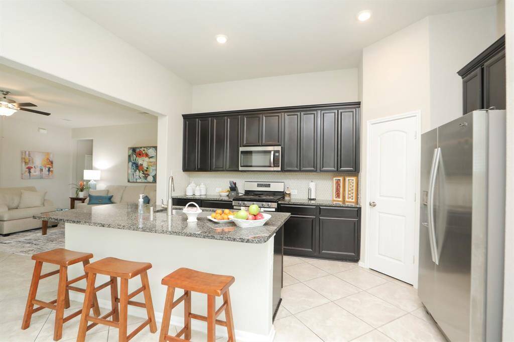 This modern kitchen with dark cabinetry, stainless steel appliances, and a large granite island with barstools. It opens into a cozy living area, creating an inviting, open-concept space ideal for entertaining.