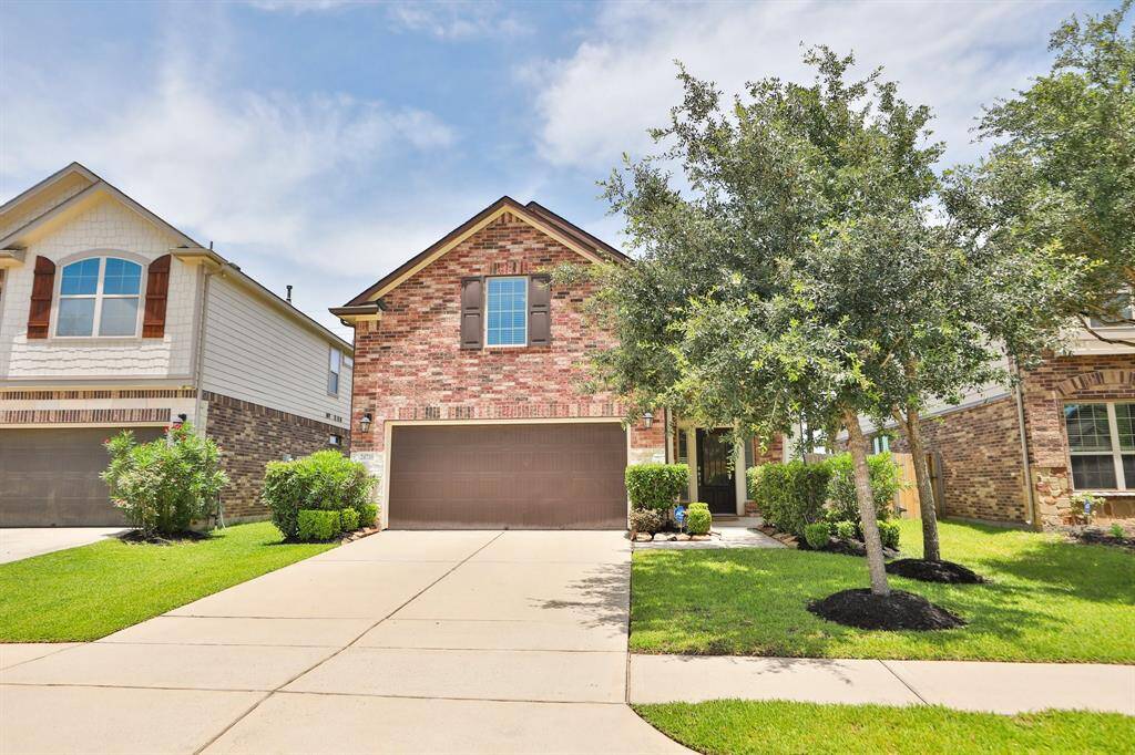 This is a charming brick house with a two-car garage and a well-maintained front yard. The property features a manicured lawn, a small tree, and some bushes, creating an inviting and attractive curb appeal.