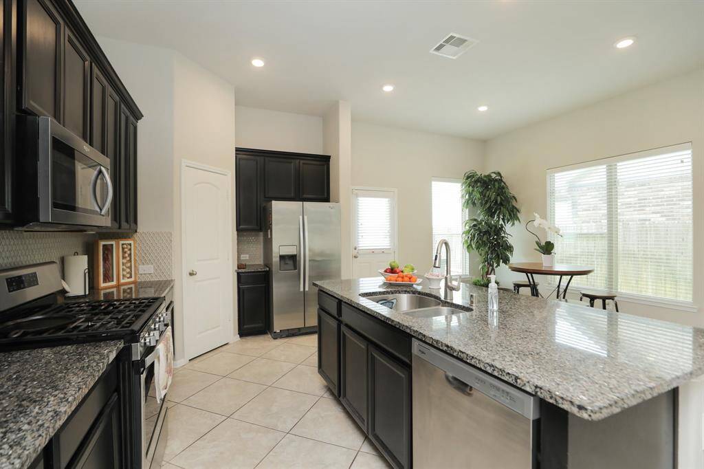 This modern kitchen features sleek dark cabinetry, stainless steel appliances, and granite countertops. A spacious island with a sink offers ample workspace, while large windows provide plenty of natural light. The open layout is perfect for dining and entertaining.