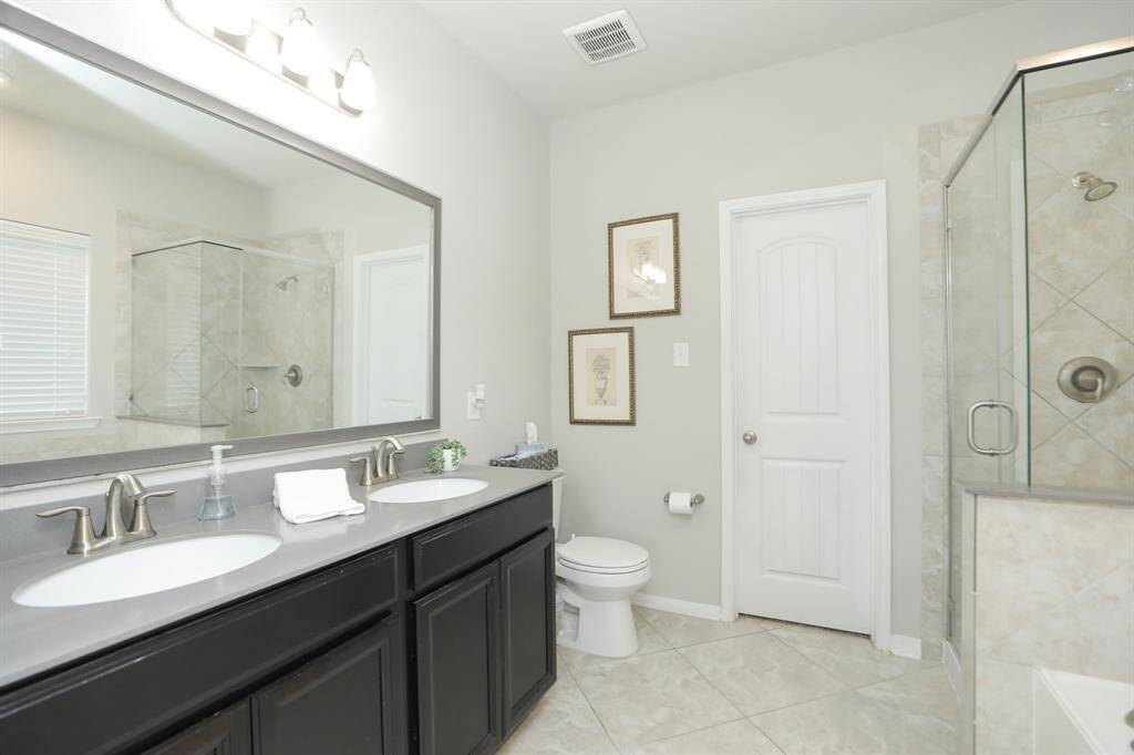 This bathroom features a modern design with a dual-sink vanity, a large mirror, and elegant fixtures. It includes a glass-enclosed shower and a neutral color palette, creating a bright and spacious feel.