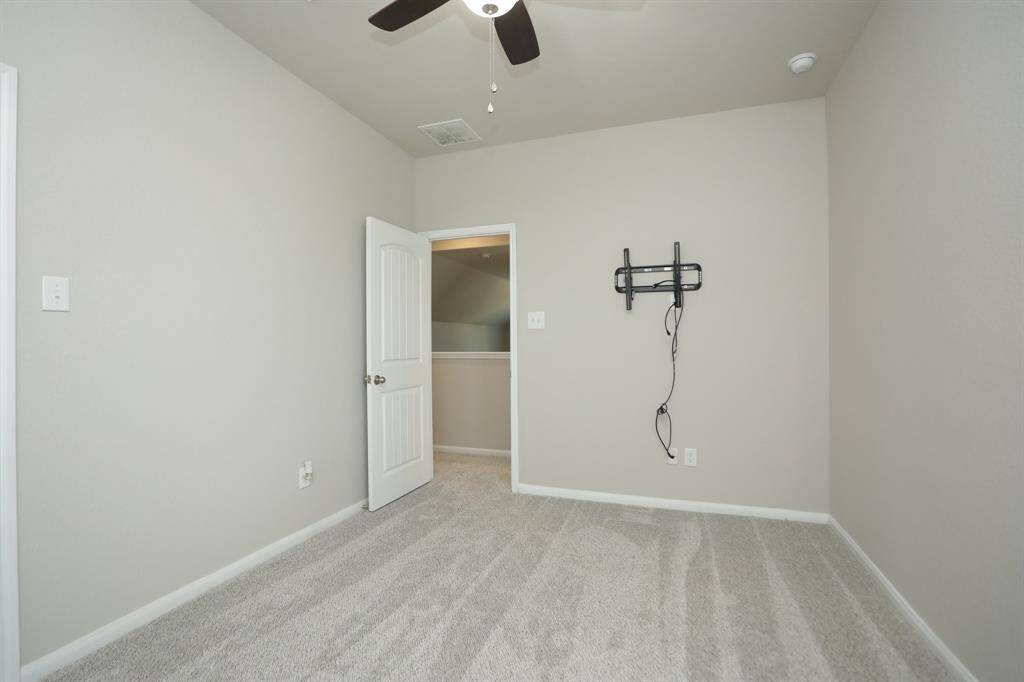 This is a nicely laid out carpeted bedroom  with neutral wall colors, featuring a ceiling fan and a wall mount for a TV.