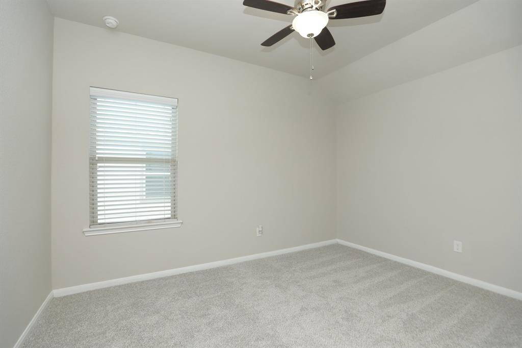 This is a bright, neutral-toned bedroom featuring a ceiling fan, a window with blinds, and plush carpeting.