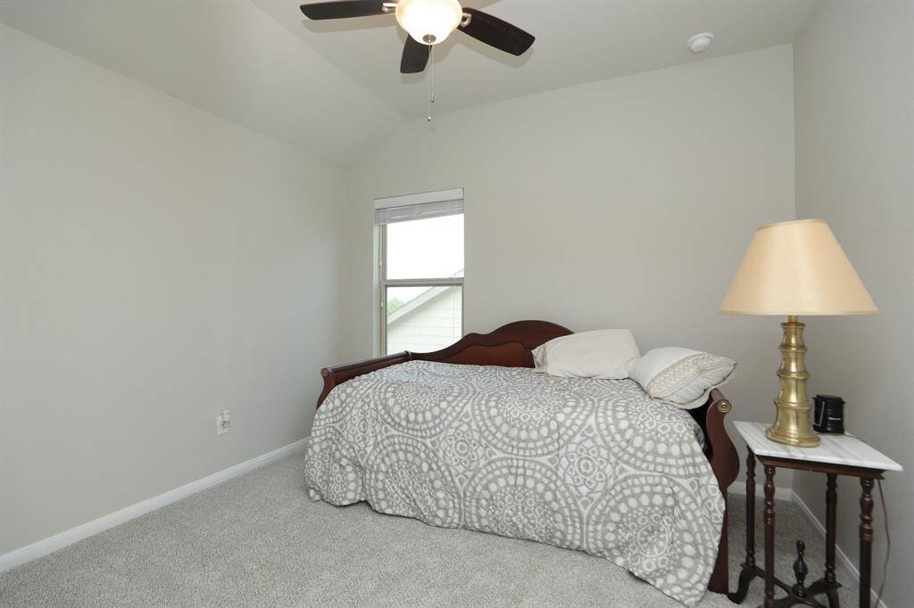 This cozy bedroom features neutral tones with a plush carpet, a ceiling fan for comfort, and a window for natural light.