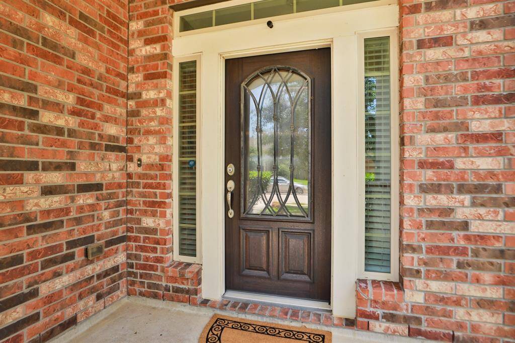 The welcoming front entrance with a stylish dark wooden door featuring decorative glass inserts. It's framed by tall side windows and set against classic red brickwork, offering a charming and inviting curb appeal.