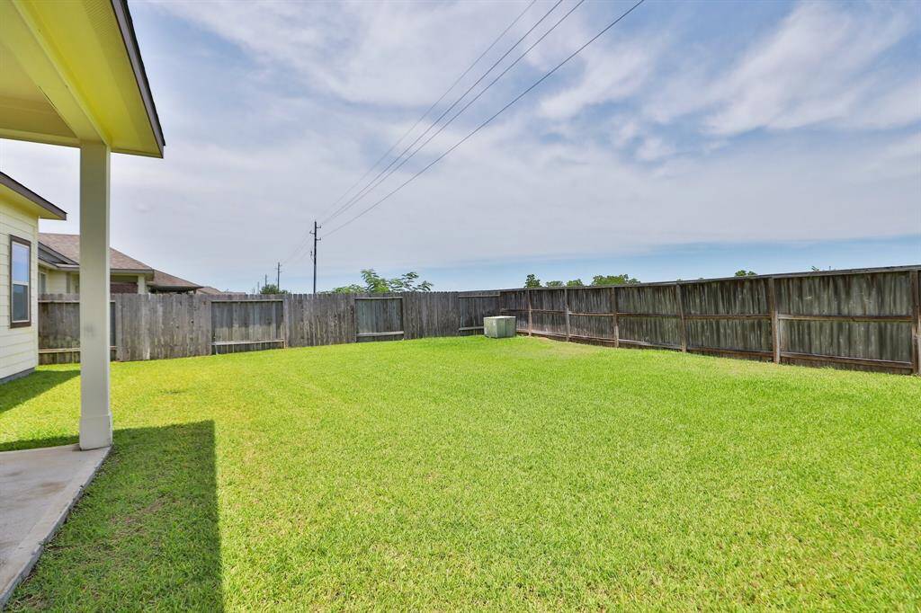 Spacious, fenced backyard with lush green grass and a small covered patio—ideal for outdoor activities and relaxation.