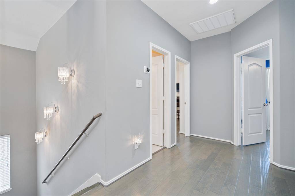 This photo shows a modern hallway with sleek hardwood floors and neutral gray walls. It features elegant wall sconces along a staircase, and multiple doorways leading to different rooms, enhancing the home's spaciousness and accessibility.