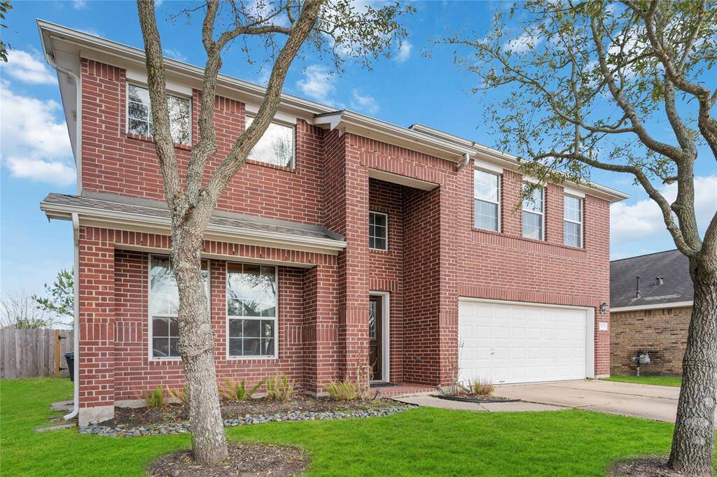 This photo showcases a two-story brick home with a clean, classic exterior. It features large windows, a two-car garage, and a well-maintained lawn with mature trees. The property exudes a welcoming and spacious feel.