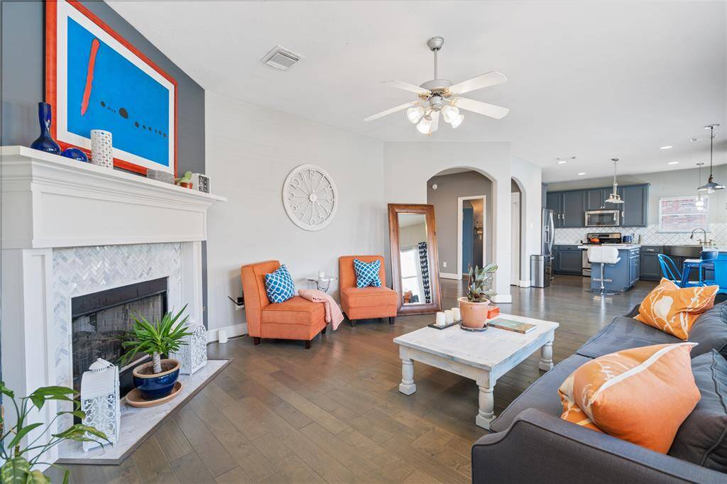 This inviting living room features a cozy fireplace, modern decor, and vibrant pops of color. It opens into a stylish kitchen with gray cabinetry and stainless steel appliances, creating a seamless flow for entertaining.