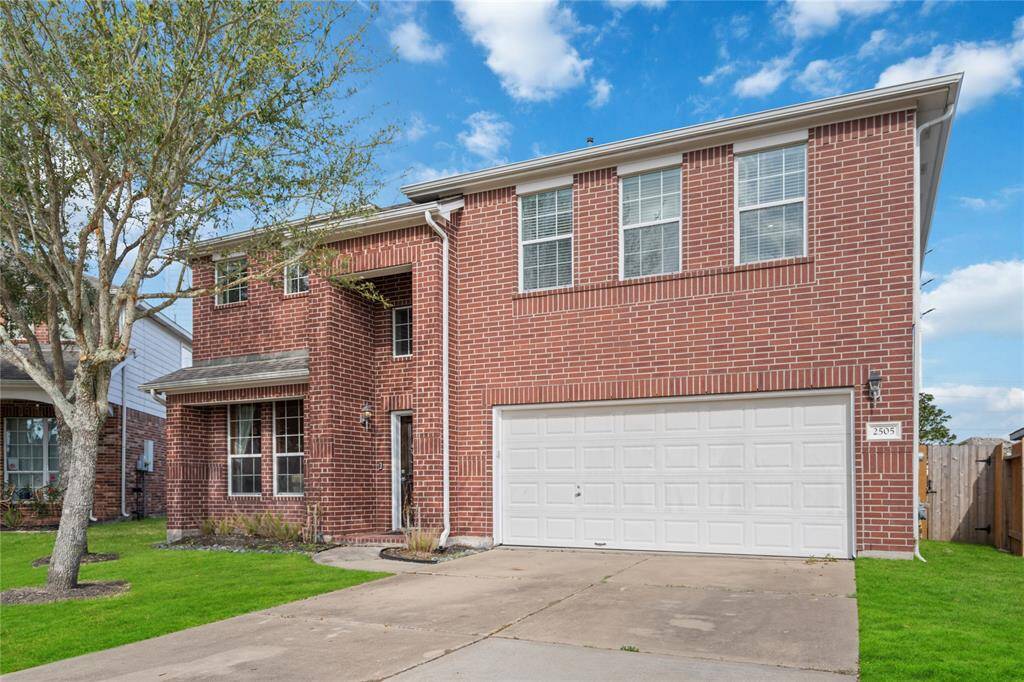 This is a two-story brick home with a large two-car garage. It features a well-maintained front lawn and a simple, elegant facade with multiple windows for natural lighting.
