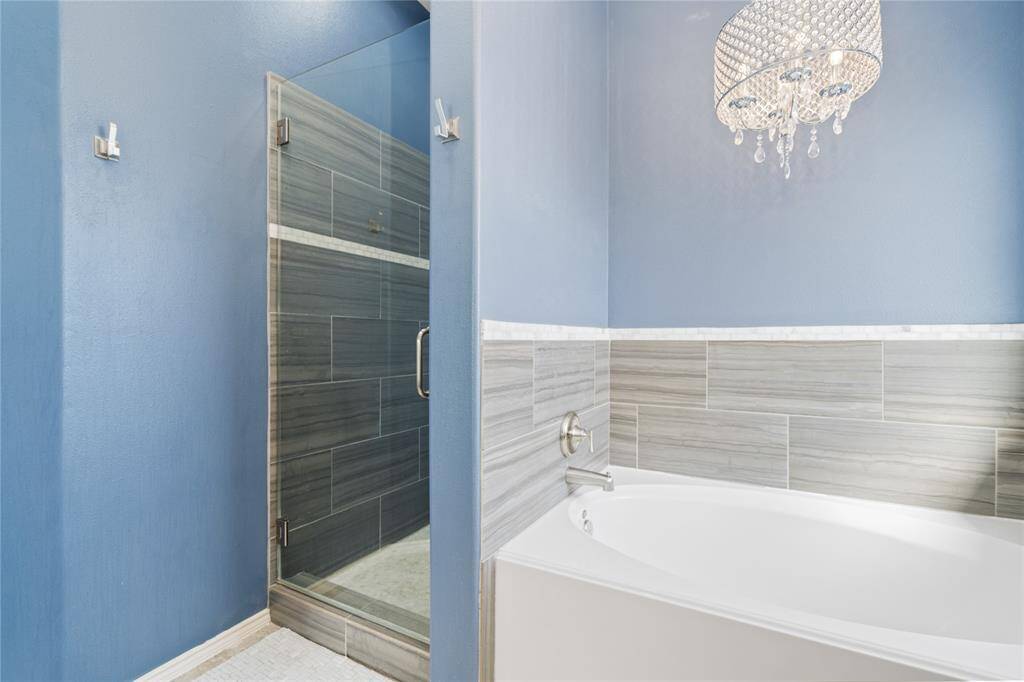 This bathroom features a sleek, modern design with blue walls, a luxurious soaking tub, and a glass-enclosed shower. The space is enhanced by elegant tile work and a chic chandelier, offering a spa-like atmosphere.