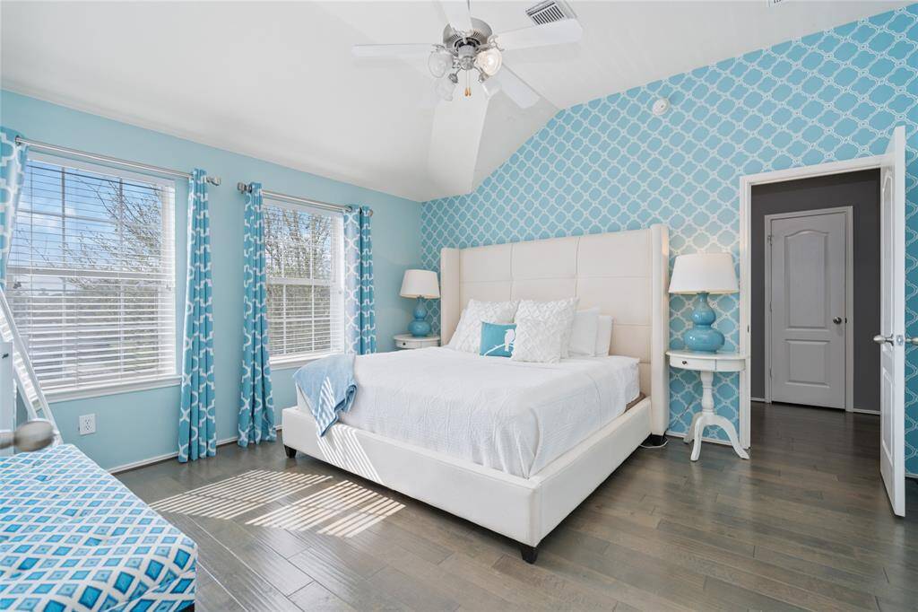 Bright, airy bedroom with a vaulted ceiling and modern decor. Features a large bed, stylish blue accents, and ample natural light from multiple windows.