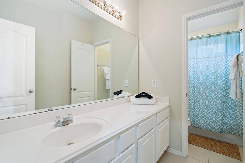This bathroom features a clean, modern design with a large mirror, ample countertop space, white cabinetry, and a bright blue patterned shower curtain for a pop of color.