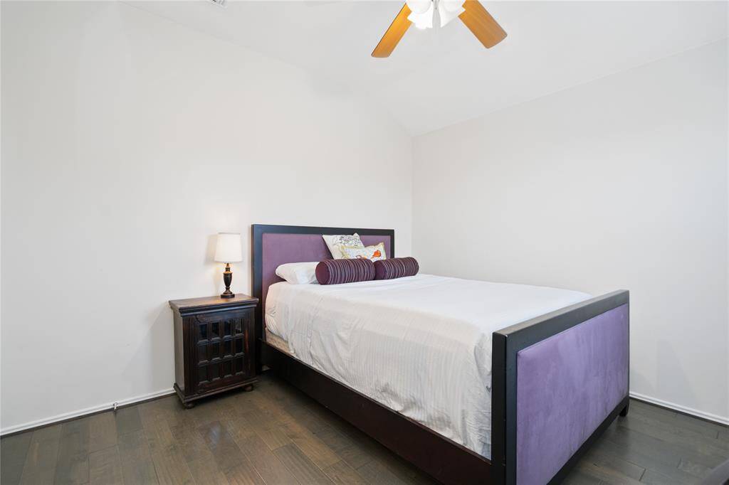 Cozy bedroom with a high ceiling, featuring a stylish bed with a purple headboard. Natural light and a ceiling fan enhance comfort, while a wooden nightstand offers practicality.