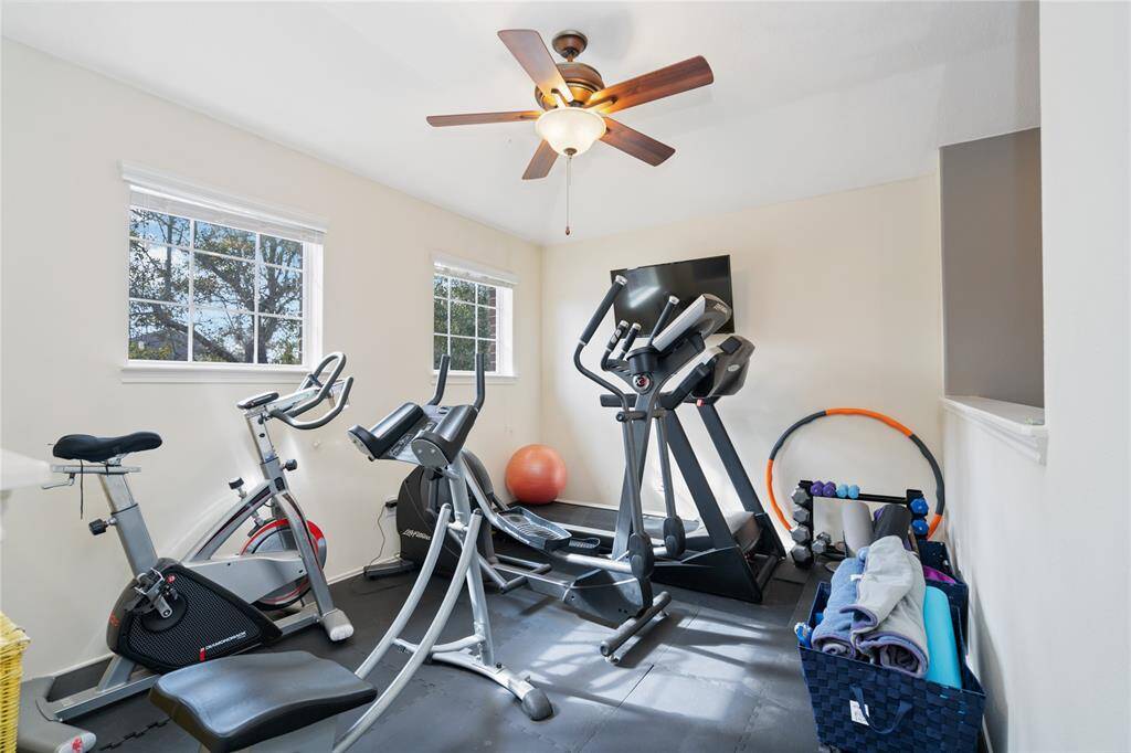 This home features a bright and functional personal gym with large windows, equipped with a treadmill, exercise bike, and fitness accessories, under a ceiling fan for ventilation.