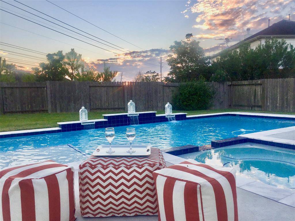 Charming backyard featuring a spacious pool with elegant water features, surrounded by a privacy fence. Enjoy outdoor relaxation with stylish seating and a picturesque sunset view.