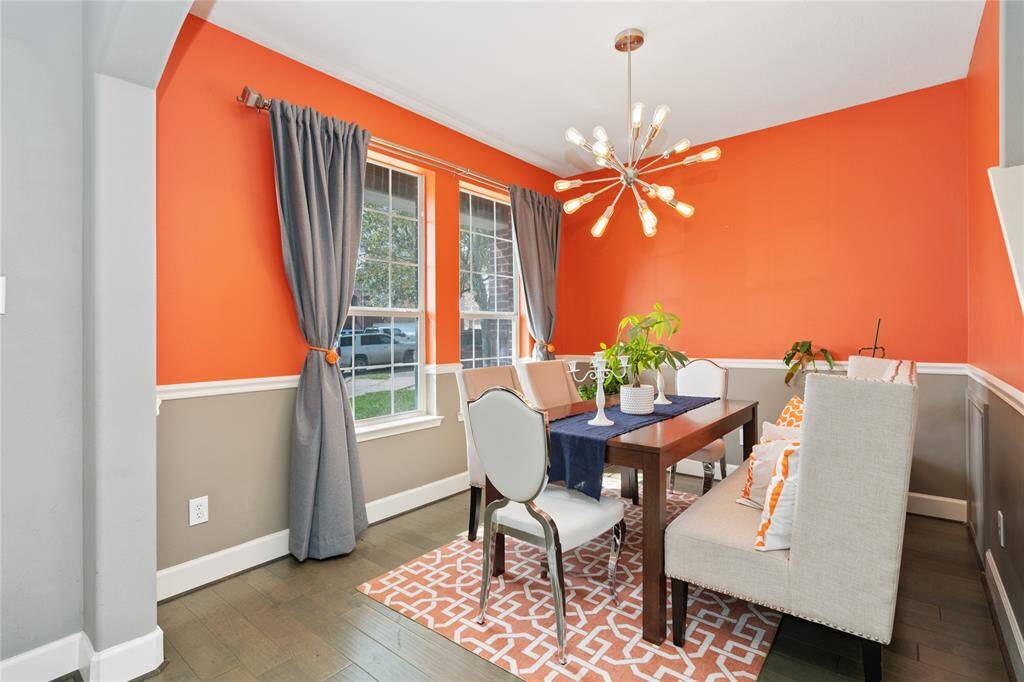 Bright dining room with bold orange walls, modern chandelier, and large windows. Features a stylish table, cushioned seating, and a patterned rug for a cozy, contemporary feel.