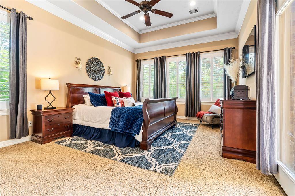 PRIMARY BEDROOM FEATURES WALLS OF WINDOWS, PLUSH CARPET, AND A BEAUTIFUL TRAY CEILING.