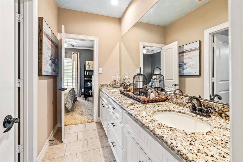 FULL BATHROOM WITH DUAL SINK VANITY, GRANITE COUNTERS, AND ACCESS TO SECONDARY BEDROOMS.