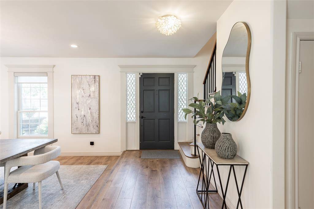 This inviting entryway features a stylish black front door framed by decorative windows. The space is bright with natural light, showcasing a modern interior with wooden floors.