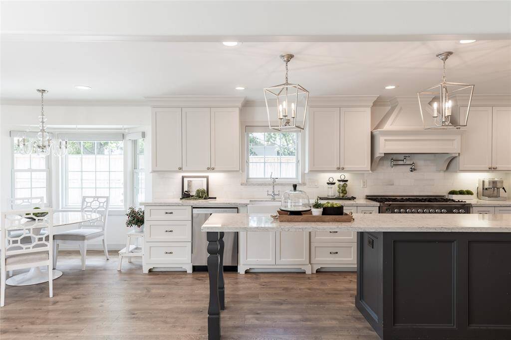 This bright, modern kitchen features white cabinetry, a large 13 ft island with pendant lighting, and stainless steel appliances. It opens to the breakfast area with a bay window, providing plenty of natural light.