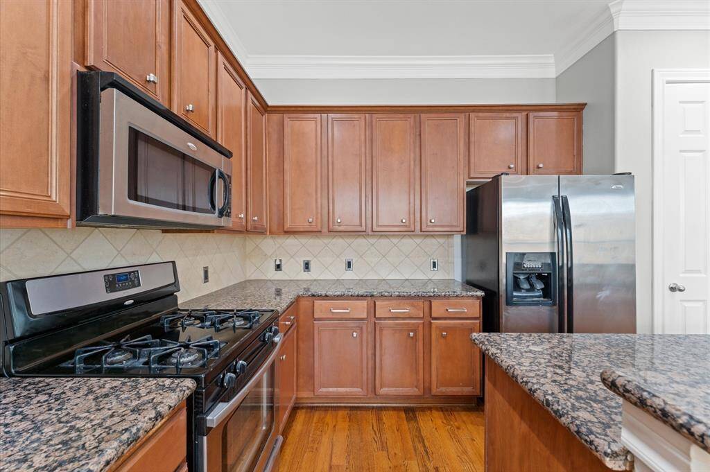 This kitchen features elegant wood cabinetry, granite countertops, and stainless steel appliances, including a gas stove and double-door refrigerator. The space is complemented by a tiled backsplash and hardwood floors, offering a warm and inviting atmosphere.