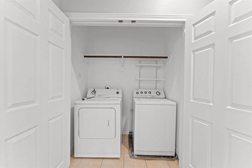 This photo shows a compact laundry closet with a washer and dryer, featuring white double doors and shelving for storage.
