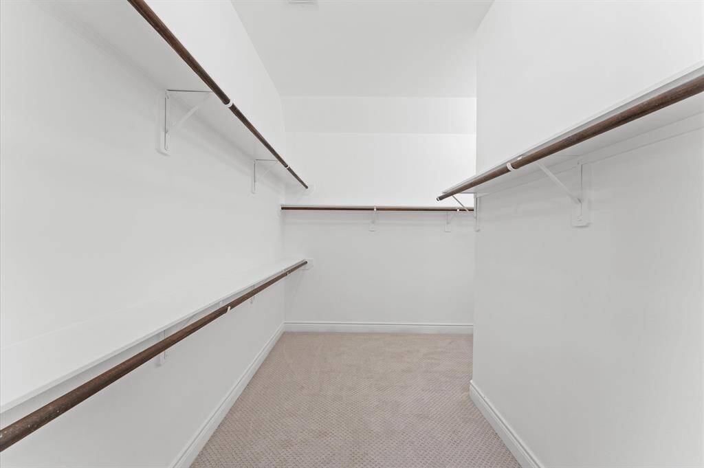 Spacious walk-in closet with ample hanging space on multiple walls, featuring white walls and carpeted flooring. Perfect for organizing clothes and accessories.