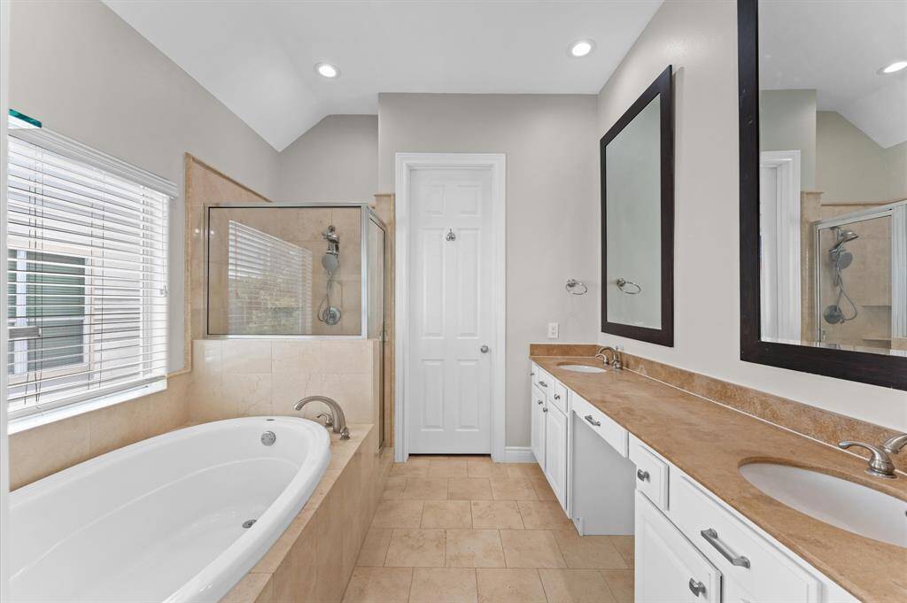 This bathroom features a spacious layout with a large soaking tub, separate glass-enclosed shower, dual sinks with ample counter space, and neutral tile and wall colors for a bright, modern feel.