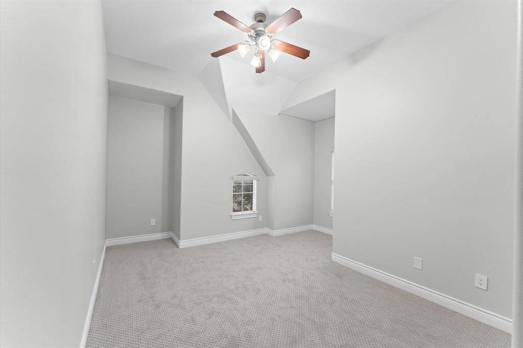This room features a neutral color palette with plush carpeting and a ceiling fan. It has unique architectural details with a small window, creating a cozy yet spacious feel.