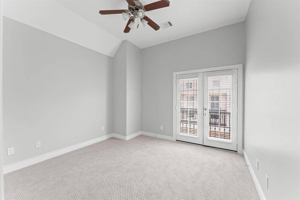 Bright room with neutral gray walls and plush carpeting, featuring a ceiling fan and double doors leading to a small balcony. Ideal for a bedroom or office space.