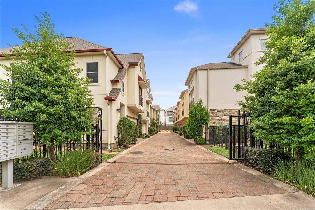 This photo shows a charming residential area with modern townhouses on either side of a paved, landscaped path. The homes feature clean lines and neutral colors, with gated entrances and greenery enhancing the welcoming atmosphere.