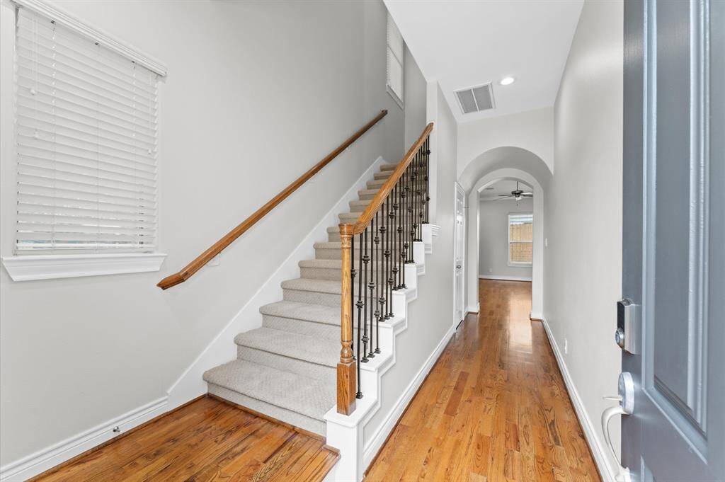 This photo showcases a bright entryway with hardwood floors, carpeted stairs with wooden and iron railings, and an archway leading to additional rooms. The space is well-lit and inviting.