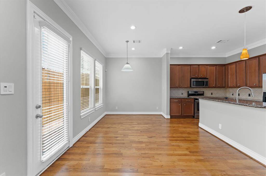 This photo showcases a bright, open-concept kitchen and dining area with hardwood floors. The kitchen features dark wood cabinets, stainless steel appliances, and a granite countertop with a breakfast bar. Large windows and a glass door provide ample natural light.
