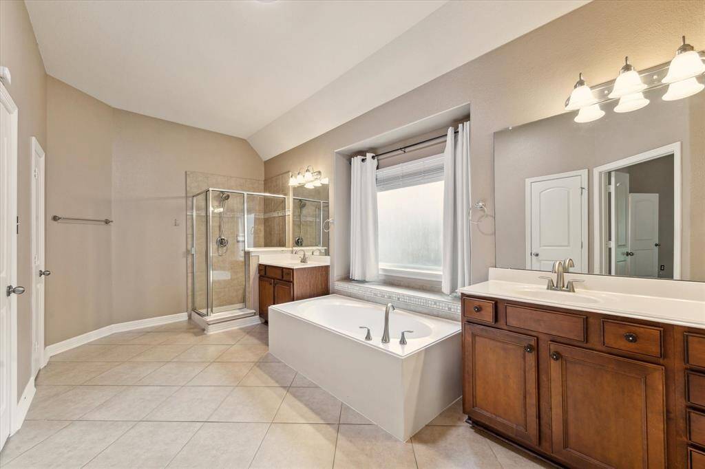 Relax and recharge in this luxurious en-suite bathroom featuring a soaking tub, separate glass-enclosed shower, dual vanities, and ample natural light.