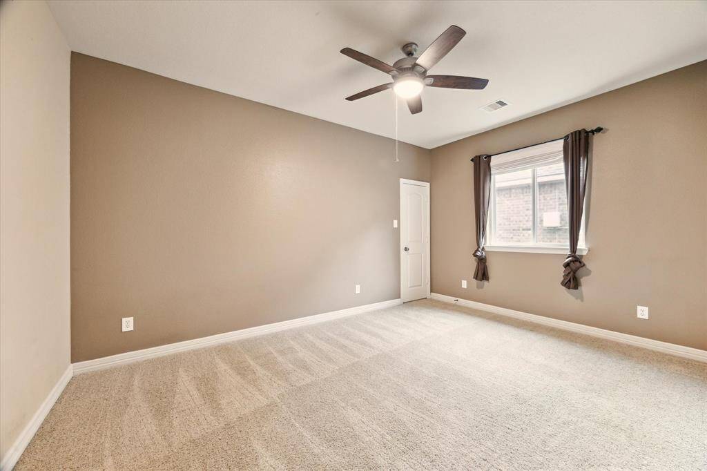 This secondary bedroom features plush carpet, a large window for natural light, neutral tones, and a modern ceiling fan. Ideal as a guest room, home office, or cozy retreat.